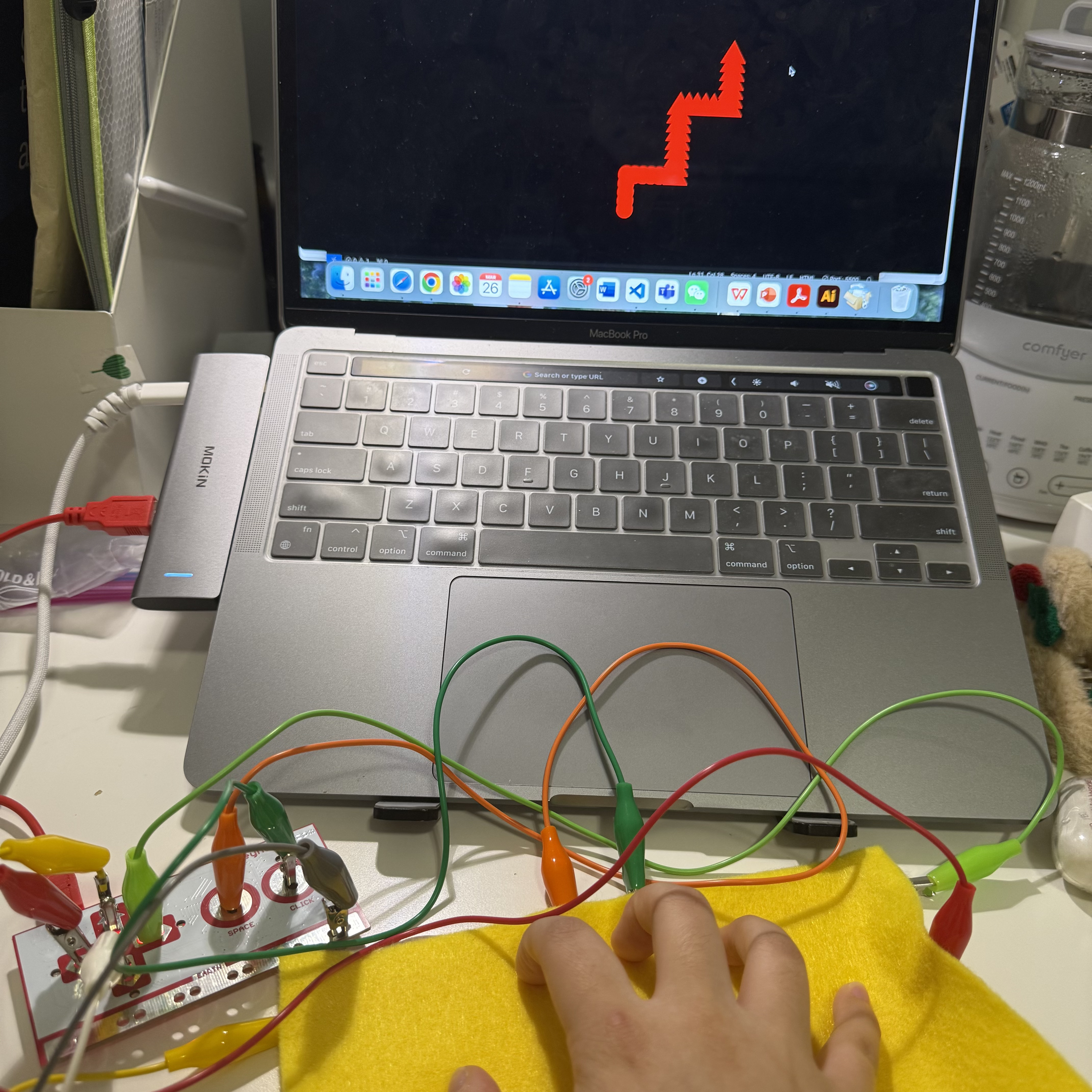 The results of my interaction are visible on the laptop screen, showing a red zigzag pattern that responds to my touches on the yellow fabric. This image captures the immediate effect of my inputs on the digital display, illustrating the potential of DIY electronics projects for interactive technology.